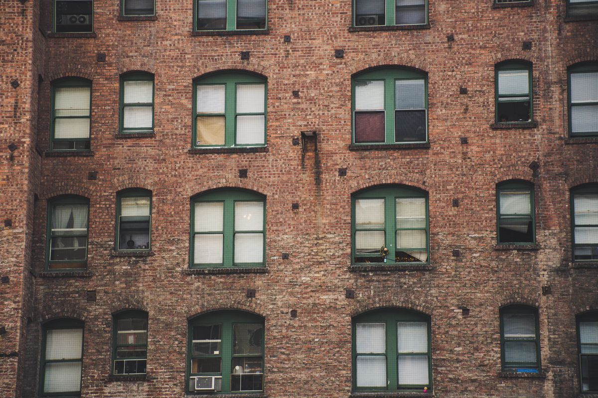 An aged brick apartment facade with a grid of green-framed windows