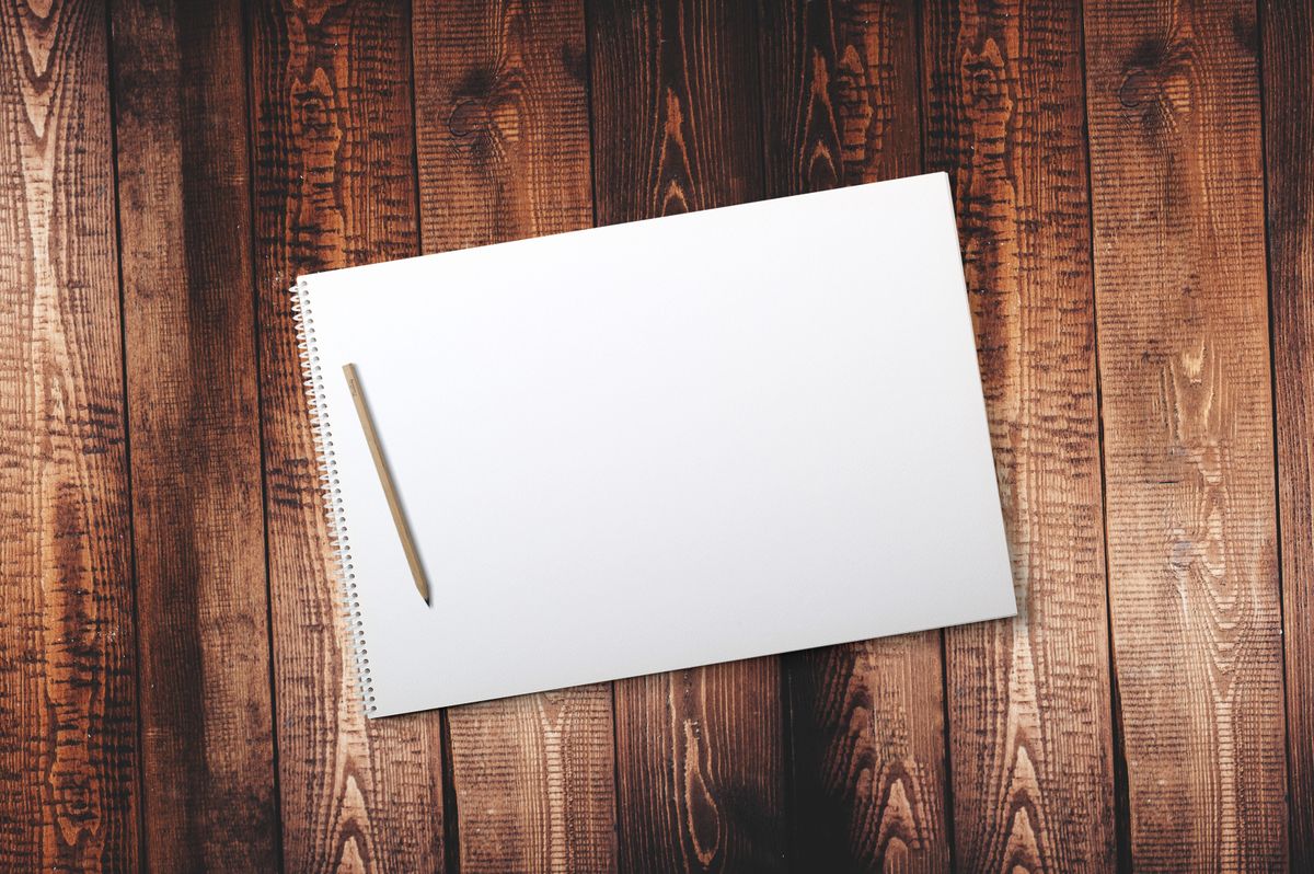 A blank spiral notepad with a single pencil on a warm timber desk