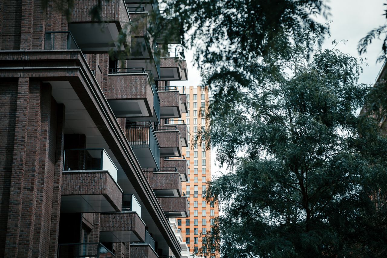 Brick apartment building with balconies beside a leafy tree under an overcast sky