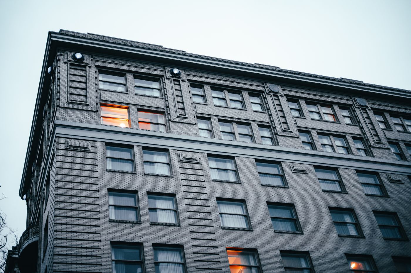A brick apartment building corner at dusk with a few warmly lit windows