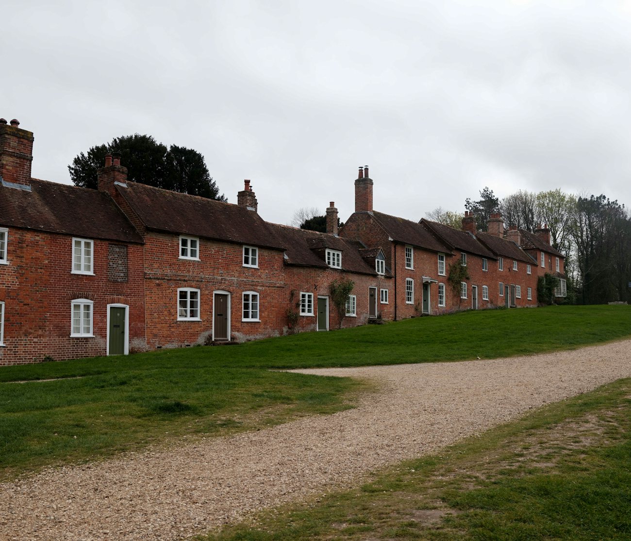 A row of brick cottages with white windows along a green under an overcast sky