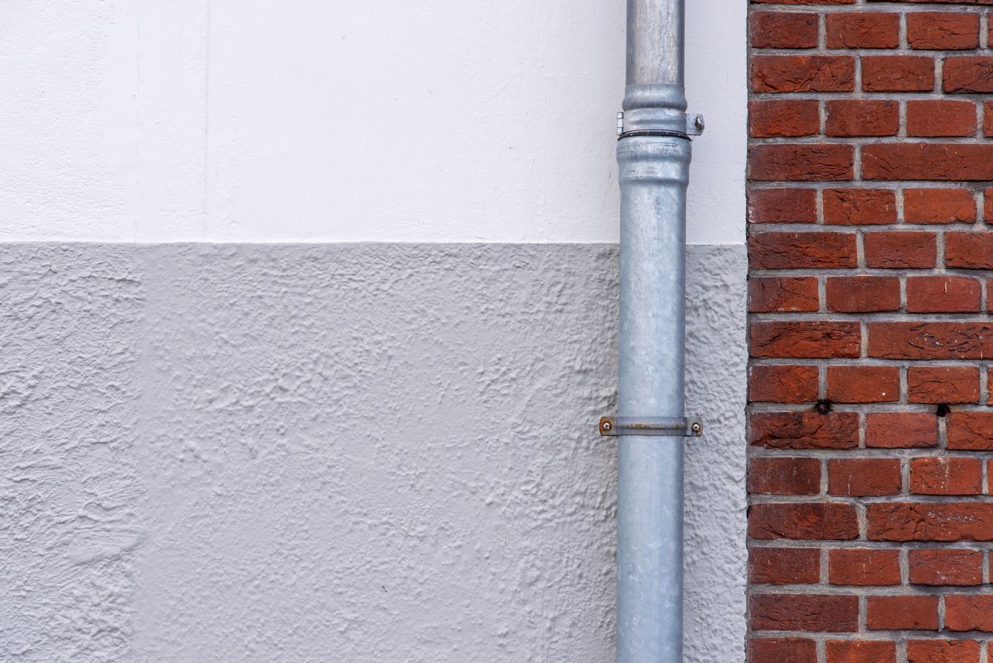 A galvanized drainpipe on a rendered wall beside a red brick facade