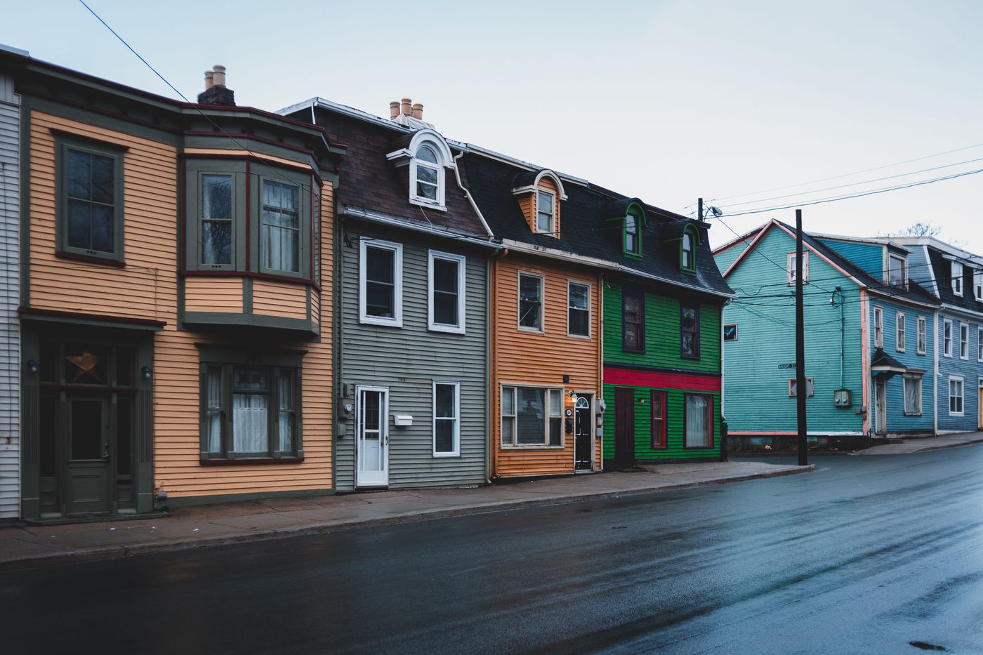 A row of clapboard houses in different colors along a wet street under an overcast sky