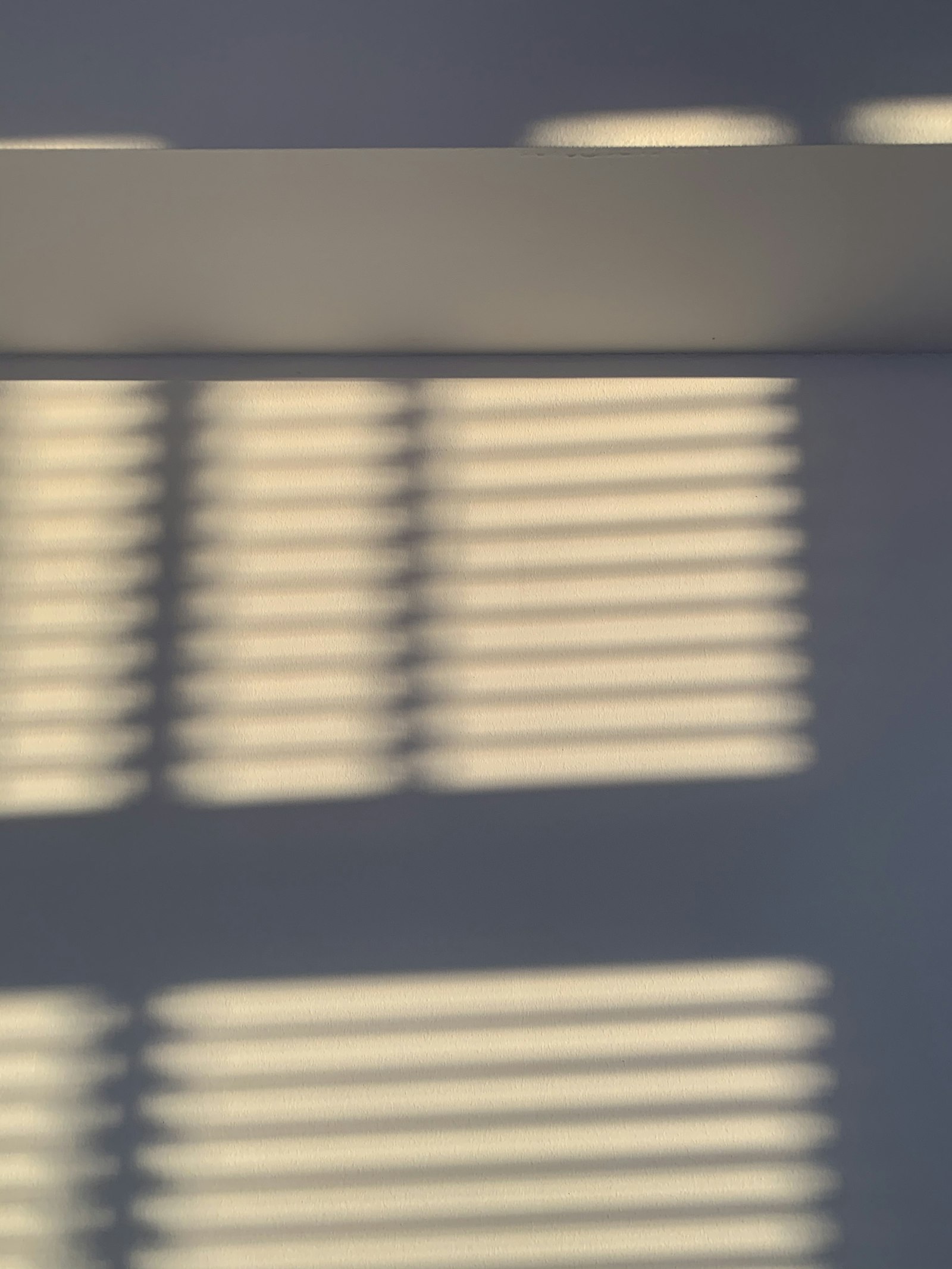 Light through window blinds falling in stripes across a pale grey wall
