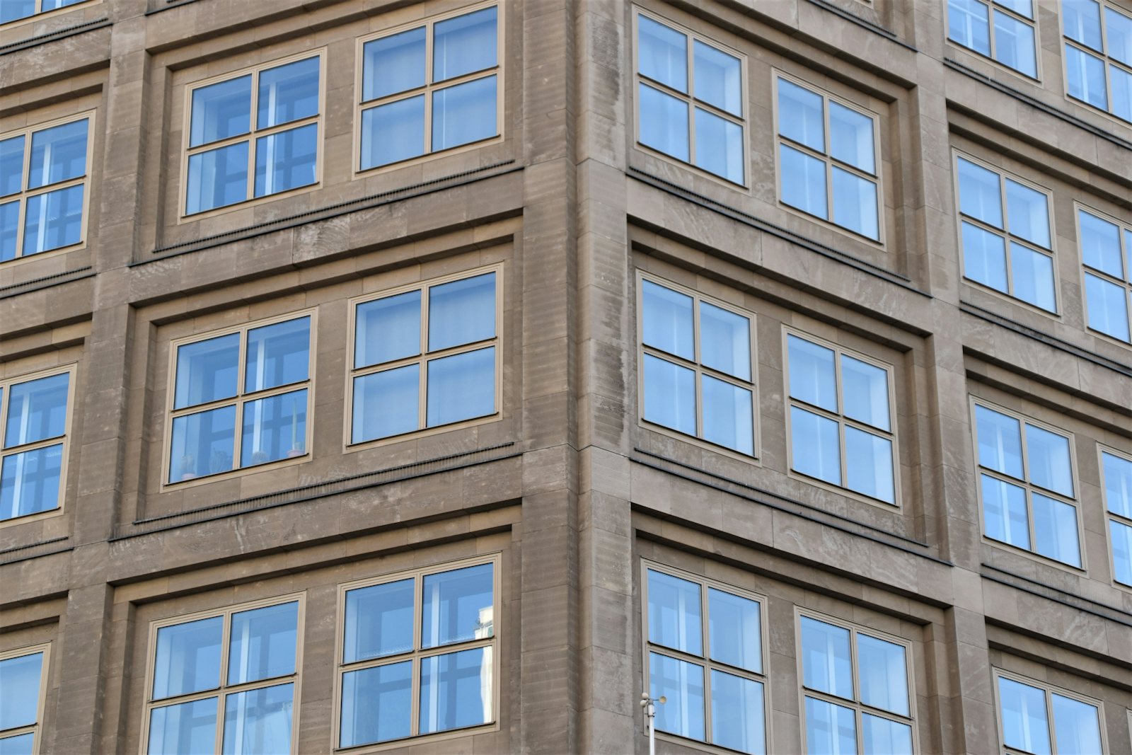 Rows of square windows set in a stone building facade, reflecting the sky