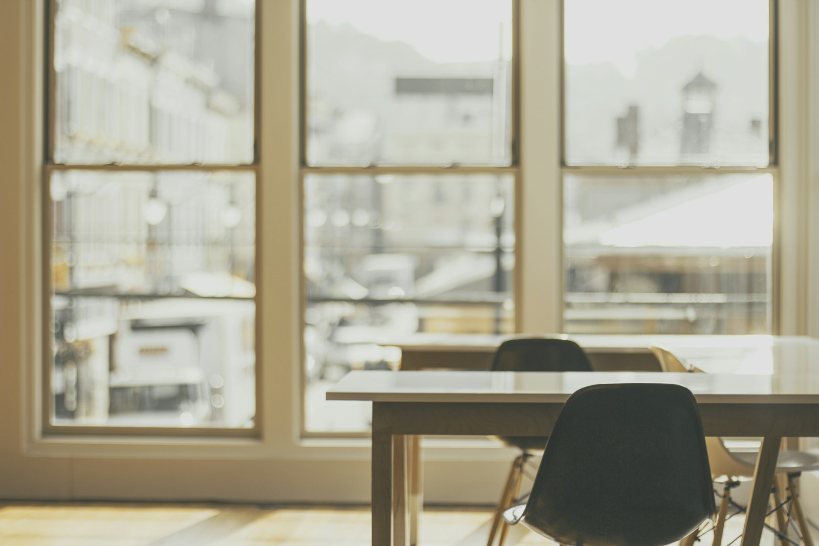 Two plain tables and chairs beside a tall window in warm morning light, the street outside out of focus