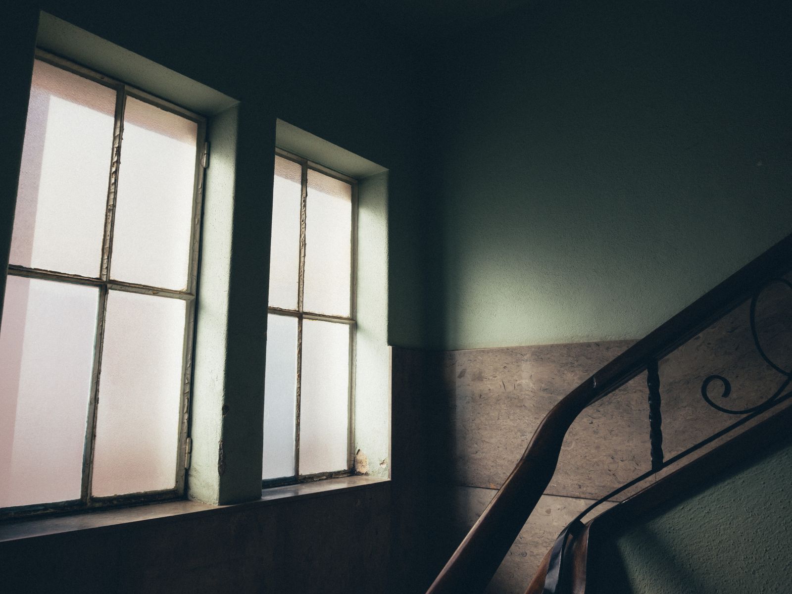 Worn staircase landing in an old apartment building with frosted windows and soft daylight